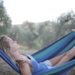 lento - A blonde woman relaxing in a hammock in a serene outdoor setting, embodying tranquility.
